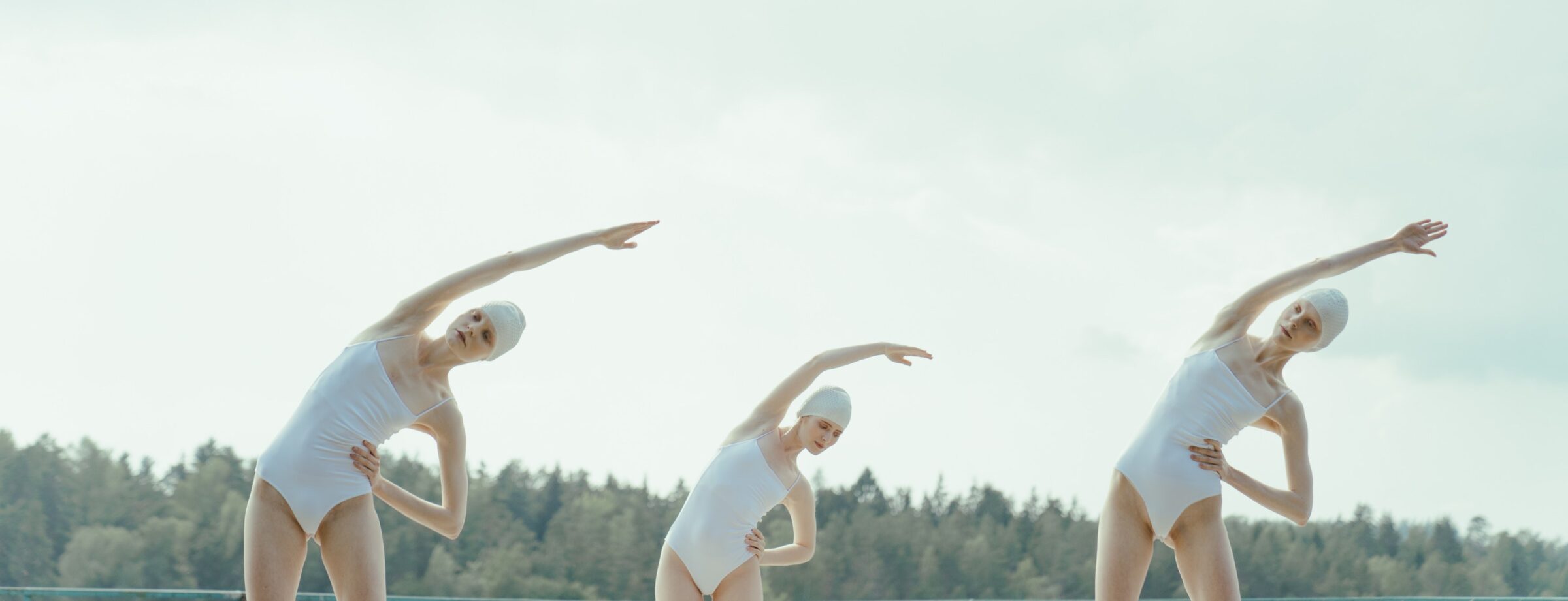 women wearing white swimsuits on a beach and stretching